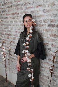 Thoughtful young woman with cotton plant standing against wall
