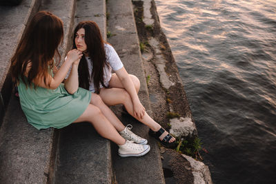 Cute lesbian couple talking while sitting on steps by river in city