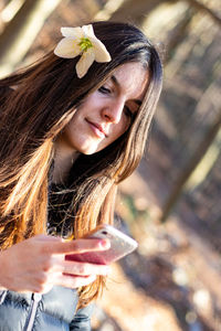 Young girl looking to her phone in the forest with white flower in her hair