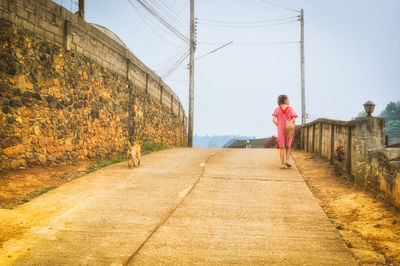 Rear view of woman walking on road against sky