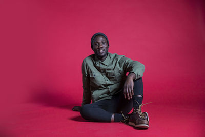 Portrait of young man sitting against pink background