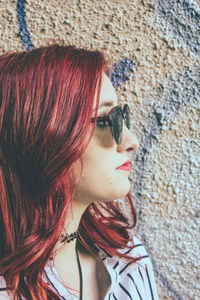 Close-up of young redhead woman wearing sunglasses by graffiti wall