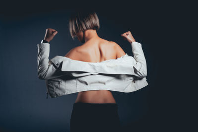 Rear view of seductive woman wearing jacket standing against black background