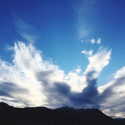 Low angle view of silhouette mountain against blue sky