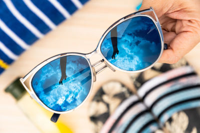 Close-up of hand holding sunglasses against blue sky