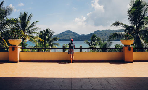 Rear view of man standing on walkway by sea against sky