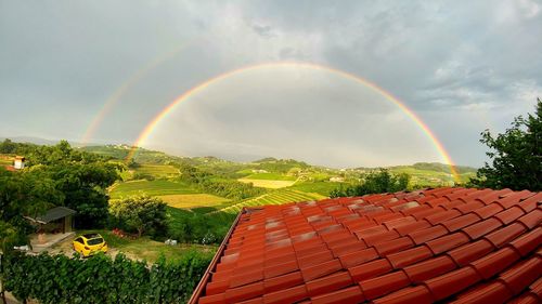 View of roof tiles with field and rainbow against cloudy sky