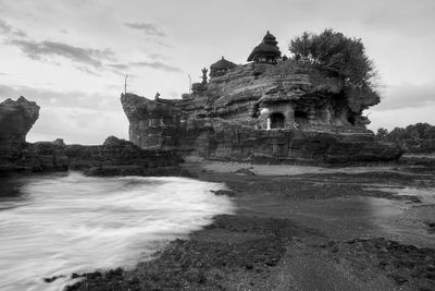 View of tanah lot rock formation against cloudy sky