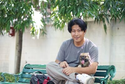 Portrait of man sitting with dog on bench at park