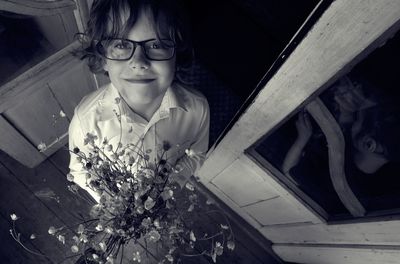 High angle portrait of smiling boy holding flowers while standing at home