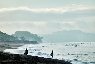 People on beach against sky in foggy morning