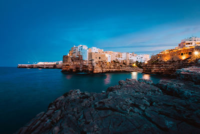 Buildings by sea against blue sky