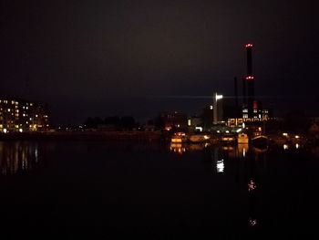 Illuminated buildings by river against sky at night