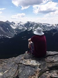 Rear view of woman sitting on rock against sky