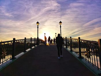 People walking on bridge against sky during sunset