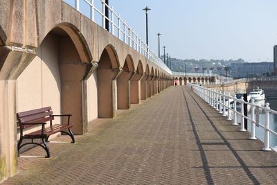 Empty benches on walkway by building against sky