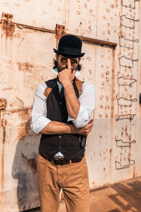 Man wearing hat standing against wall