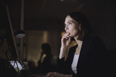 Mature businesswoman with hand on chin working over computer at work place