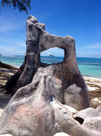 Driftwood on rocks by sea against blue sky