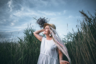 Girl with bright braids in straw hat holding bouquet of flowers, wind in nature