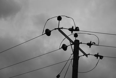 Low angle view of electricity pylon against cloudy sky