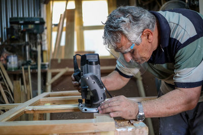 An adult man wearing face mask while working on wood in the shed. 