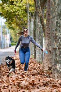 Full length of woman wearing mask running with dog standing in forest