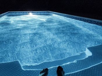 Low section of person dangling feet in swimming pool