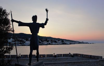 Rear view of man standing by sea against sky during sunset