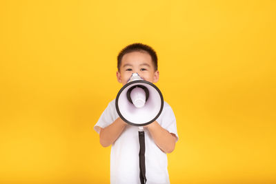 Portrait of boy holding camera against yellow background