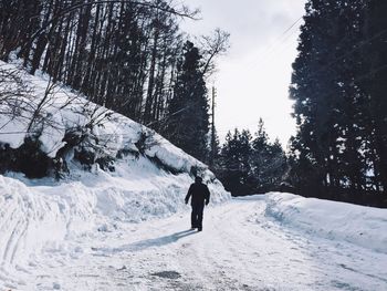 Rear view of man walking on snow against sky