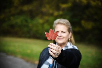 Smiling woman holding maple leaf during autumn