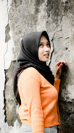 Portrait of smiling young woman standing against wall