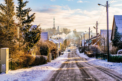 Snow covered road amidst buildings in city