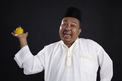 Portrait of man holding container while standing against black background