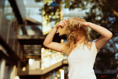 Woman with tousled hair standing against tree and buildings