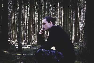 Side view of man sitting on tree trunk in forest