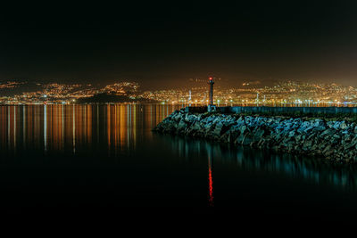 Illuminated buildings by sea against clear sky at night