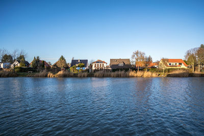 Houses by sea against clear blue sky