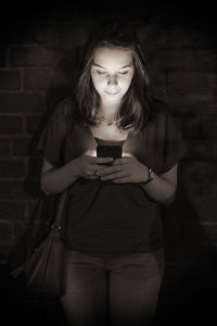 Beautiful woman text messaging against brick wall at night