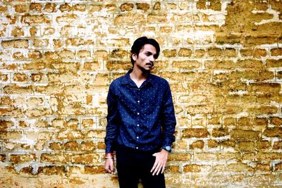 Portrait of young man standing against brick wall