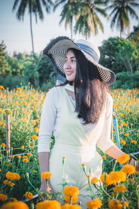 Young woman wearing hat while standing amidst flowers on field