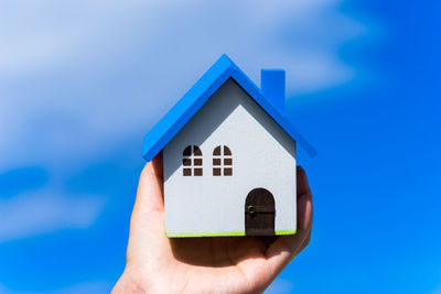 Cropped image of hand holding model home against blue sky