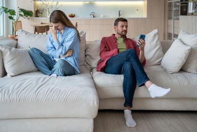 Sad crying wife regretting of marriage, thinking of divorce, and egoistic man addicted to smartphone