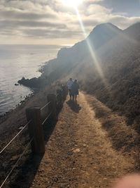 Rear view of people walking on mountain by sea against sky
