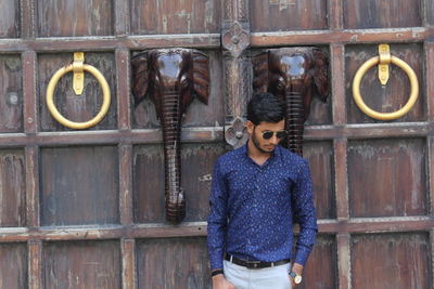 Man wearing sunglasses standing by wooden door