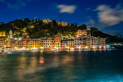 Buildings by river against sky at night