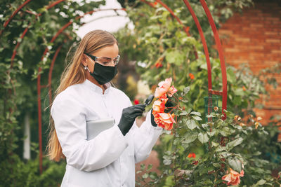 Young woman holding umbrella while standing by flowering plants