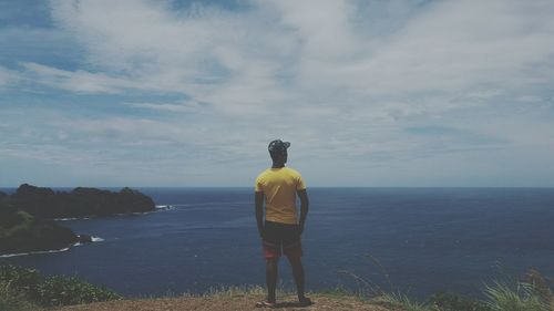 Rear view of man standing at beach against sky