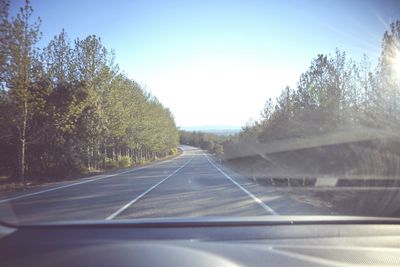 Road amidst trees against clear sky seen through car windshield